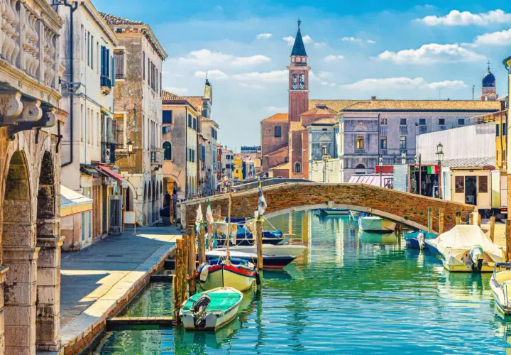 Un rêve d'aller à Venise : un canal bordé de maisons anciennes, un pont de briques et des gondoles.