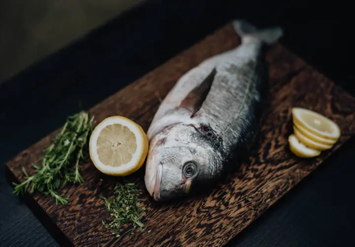 Un beau daurade prêt à être grillé, accompagné de citron frais et de romarin sur une planche en bois.