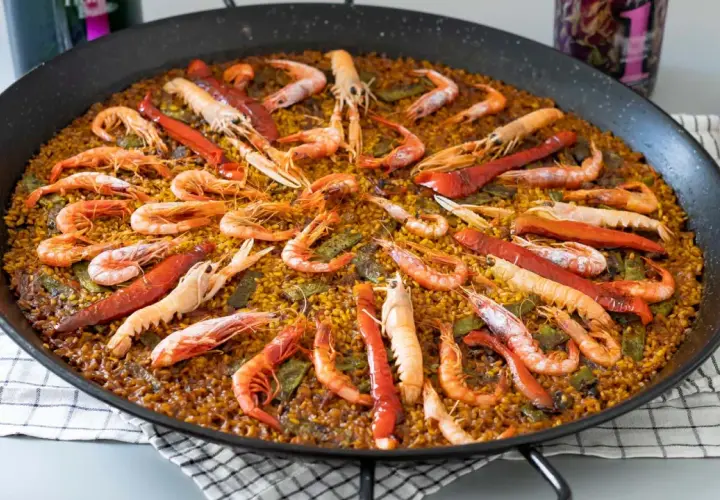 Paella gigante con gambas y pimientos rojos, perfecta para compartir. Cada porción de arroz está llena de sabor.