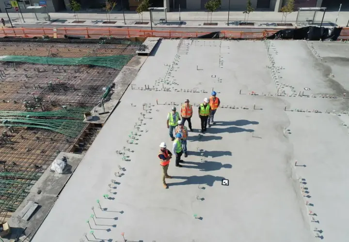 Grupa budowlańców na placu budowy. Zastanawiają się, ile kosztuje kubik betonu, patrząc na zbrojenie i świeżo wylany beton.