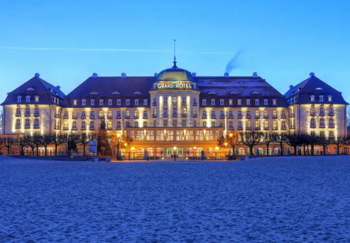 Grand Hotel w Sopocie, jeden z najpiękniejszych hoteli w Polsce, lśni nocą nad piaszczystą plażą.