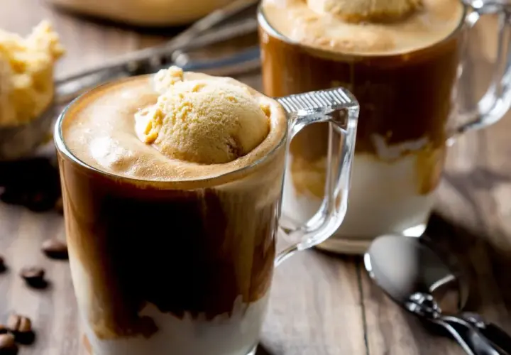 Dwa kubki caffe freddo z gałką lodów waniliowych na wierzchu, na drewnianym stole, obok ziaren kawy.