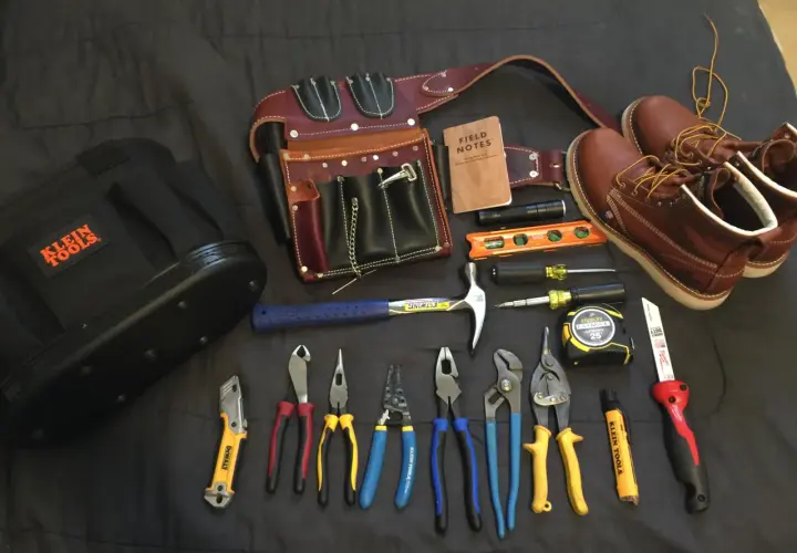 Un cinturón de cuero con múltiples compartimentos, un martillo, alicates, destornilladores, cinta métrica y botas de trabajo. Todo listo para un electricista.