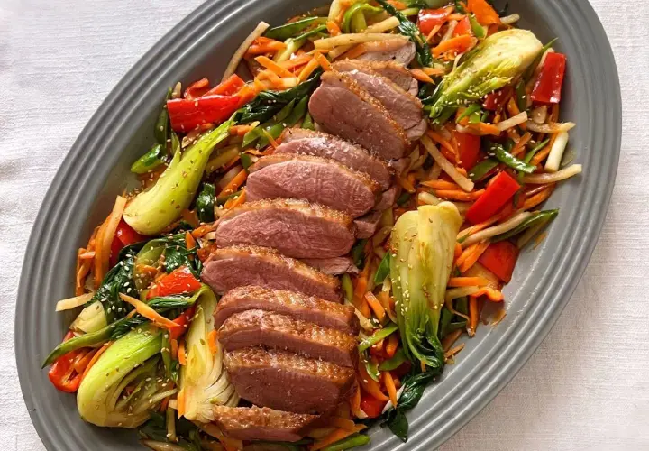 Skivad confiterad anka serveras med en färgstark wok av grönsaker som pak choi, morötter och paprika, toppad med sesamfrön.