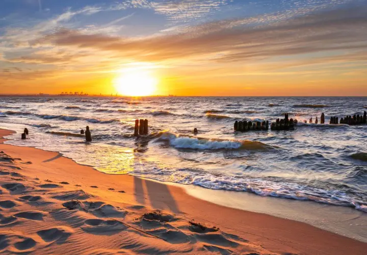 Zachód słońca nad Bałtykiem. Piasek na plaży, fale rozbijające się o pozostałości falochronów. Piękne wybrzeże polski.