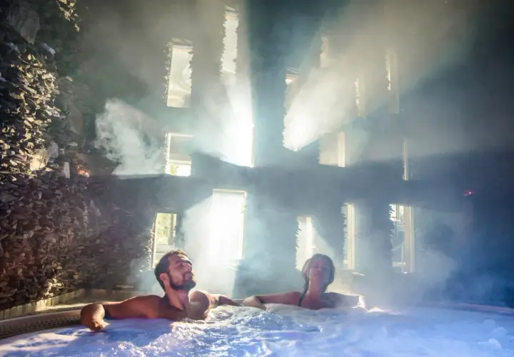 Para spędza relaksujący weekend we dwoje w jacuzzi, otoczona parą i światłem wpadającym przez okna.