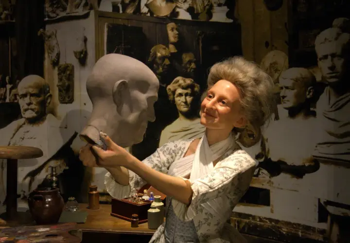 W muzeum figur woskowych artystka w historycznym stroju pracuje nad popiersiem.