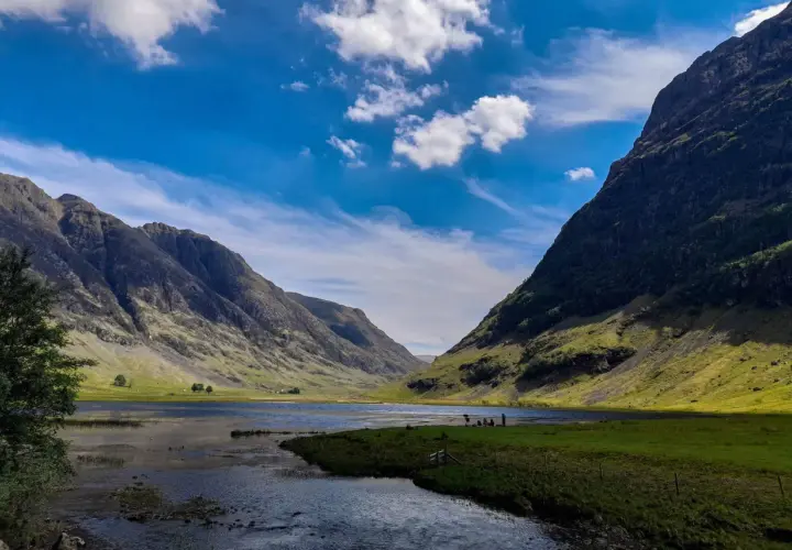 Un paisaje espectacular para hacer **escocia en bicicleta**. Montañas verdes, un lago sereno y un cielo azul con nubes.