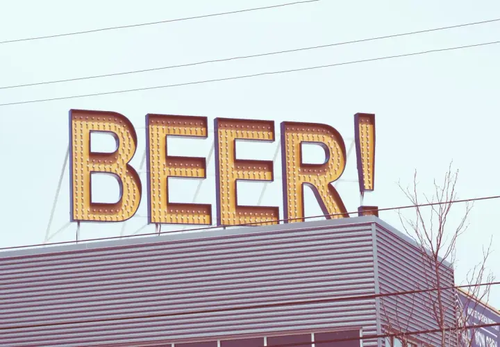 Grand panneau lumineux "BEER!" au-dessus d'un bâtiment moderne. Le nom de bière est écrit en lettres majuscules, illuminées par des ampoules.