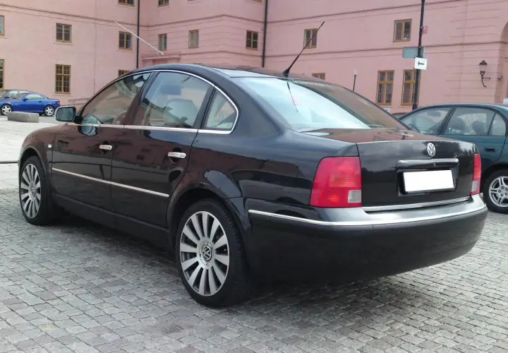 Svart Passat W8 parkerad på kullerstensgata framför en rosa byggnad.