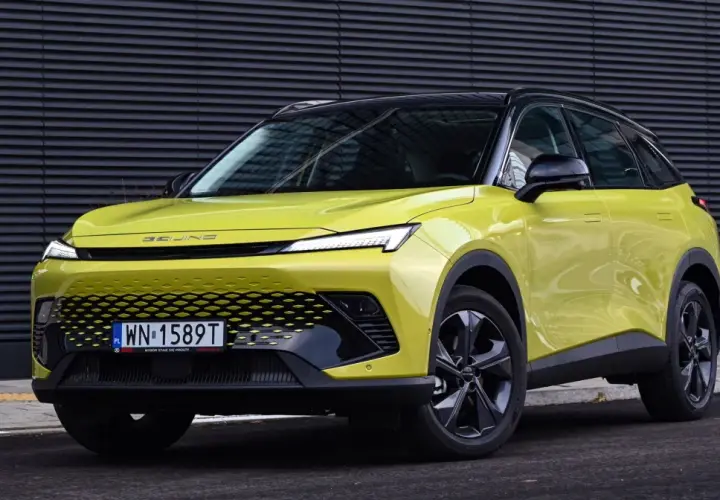 Jasnozielony BAIC 5 z czarnym dachem, nowoczesnym grillem i LED-owymi światłami, zaparkowany przed ciemną, falistą ścianą.