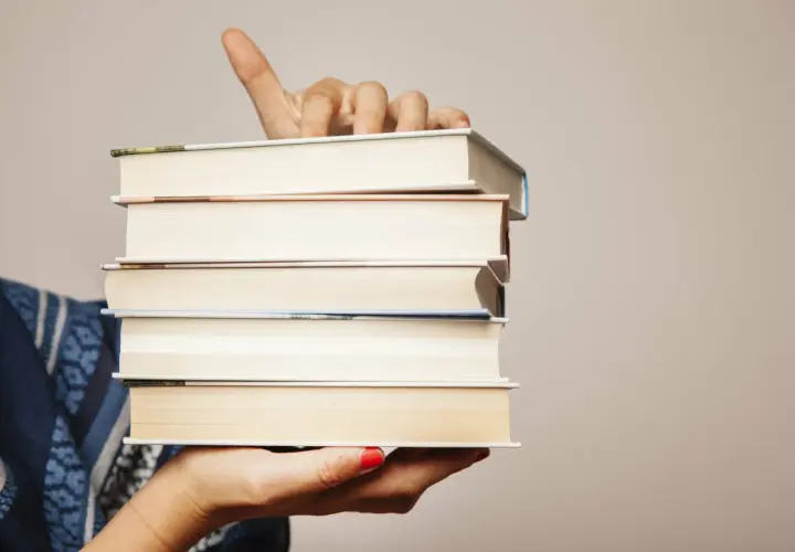 Main tenant une pile de livres, le doigt levé comme pour indiquer un titre. Chaque livre a son propre isbn.