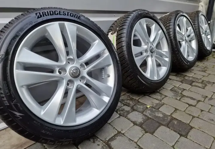 Cztery felgi aluminiowe z oponami zimowymi Bridgestone, z logo Opla, stojące na bruku.