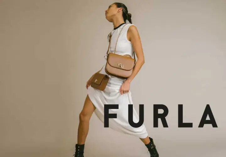 Modelka w białej sukience prezentuje dwie brązowe torebki Furla, symbol tanich włoskich marek.