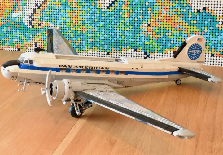Ein detailreiches Lego DC-3 Flugzeug der Pan Am steht auf einem Holzboden, im Hintergrund eine bunte Lego-Weltkarte.