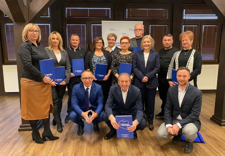 Grupa osób pozuje do zdjęcia z niebieskimi folderami. Na folderach widnieje napis "Platforma Obywatelska".