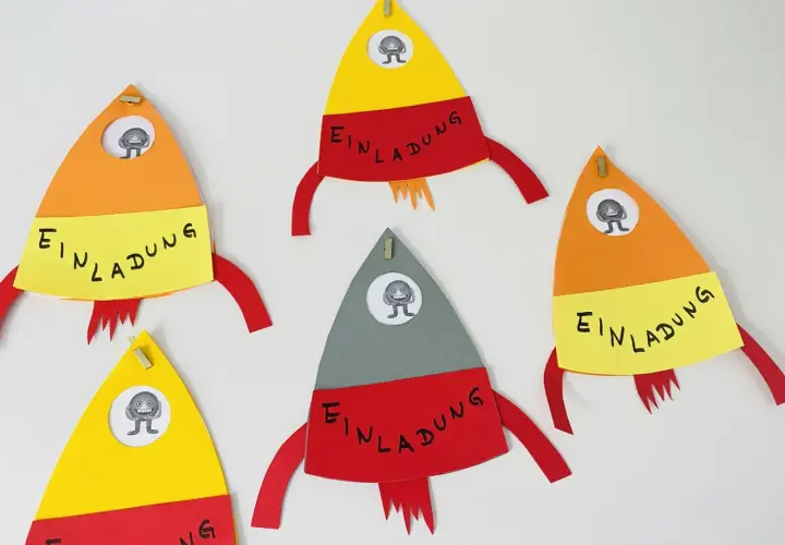Bunte Raketen zum raketen einladung basteln, jede mit einem kleinen Monster im Fenster und dem Wort "Einladung" auf gelbem Band.