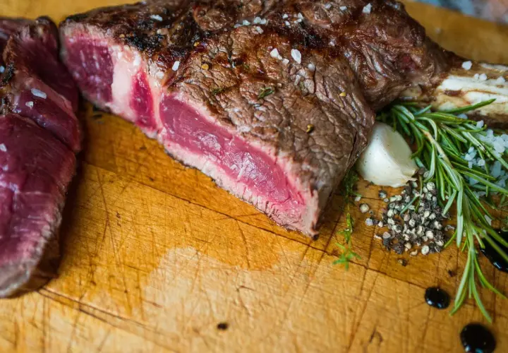 Une belle côte de bœuf de 1,2 kg, parfaitement saisie, prête pour la cuisson. Sel, poivre, ail et romarin accompagnent cette pièce de viande juteuse.
