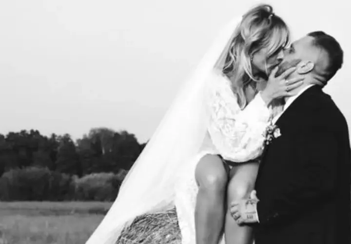 Patrycja Markowska i jej mąż w czułym uścisku na tle wiejskiego krajobrazu.