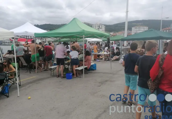 Gente reunida bajo carpas en un evento al aire libre en **Santa Ana, Castro Urdiales**. Un día nublado con ambiente festivo.
