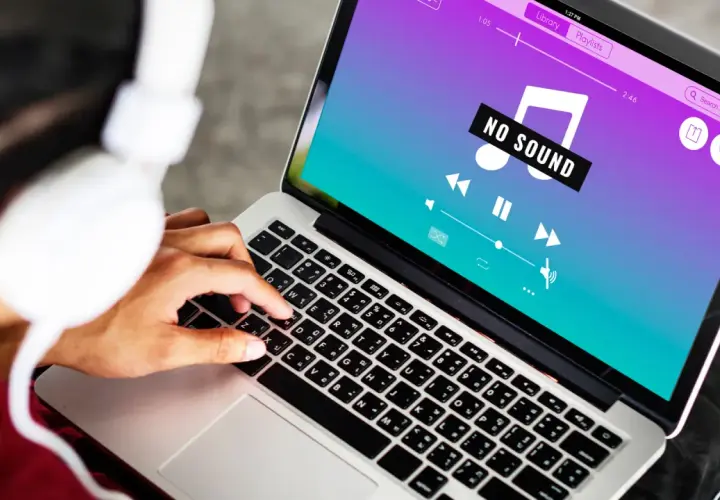 Osoba w słuchawkach próbuje rozwiązać problem **braku dźwięku w laptopie**, na ekranie widnieje komunikat "NO SOUND".