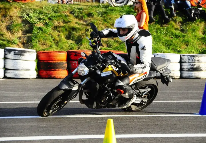 Motocyklista w białym kasku i kombinezonie doskonale opanował pozycję na motocyklu, pochylając się na zakręcie toru.