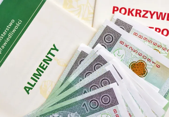 Dokumenty i banknoty 100 zł. Widoczne napisy "ALIMENTY" i "POKRZYWDZONY". Symbolizuje to, jak komornik przelewa alimenty.