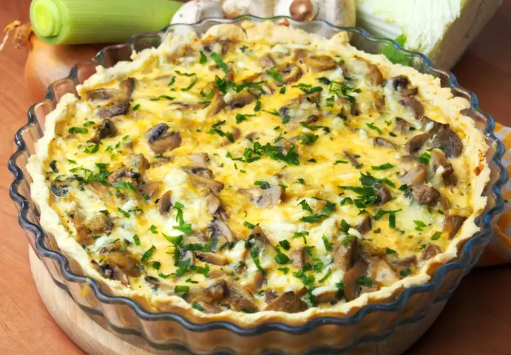 Pyszna tarta z pieczarkami i porem, posypana świeżą natką pietruszki, w szklanej formie.