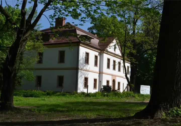 Dworek otoczony drzewami. Jak sprawdzić czy budynek jest zabytkiem? Sprawdź tablicę informacyjną obok.