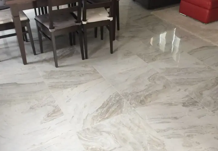 Pavimento in gres porcellanato effetto marmo, con venature grigie e bianche, sotto un tavolo con sedie scure.