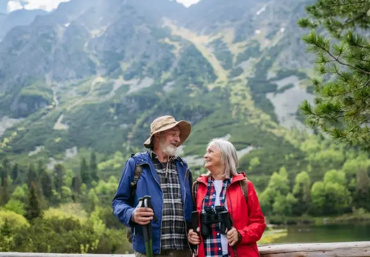Szczęśliwa para seniorów na wczasach ze związku emerytów, podziwiająca górski krajobraz z jeziorem.