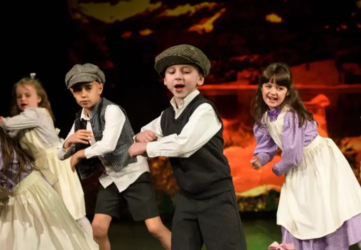 Dzieci w strojach teatralnych tańczą na scenie.