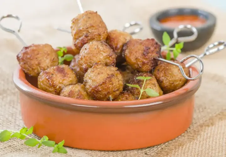Polpette di tacchino dorate e succulente, cotte nella friggitrice ad aria, servite in una ciotola di terracotta con erbe aromatiche.