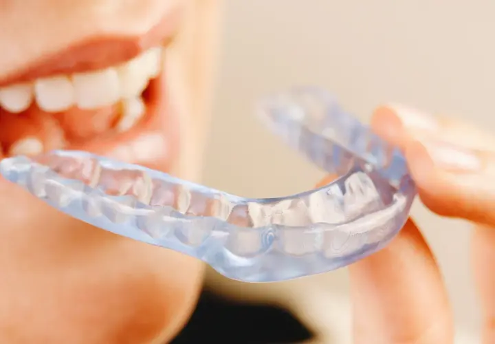 Persona sonriente sostiene una férula Invisalign transparente, lista para mejorar su sonrisa.