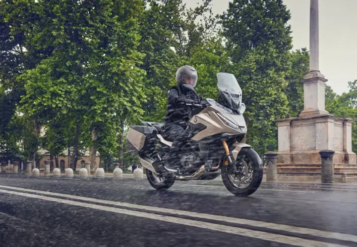 Motociclista en moto beige con alforjas, rodando bajo la lluvia. ¿Cuántos kilómetros dura una moto 125? ¡Esta parece lista para un largo viaje!