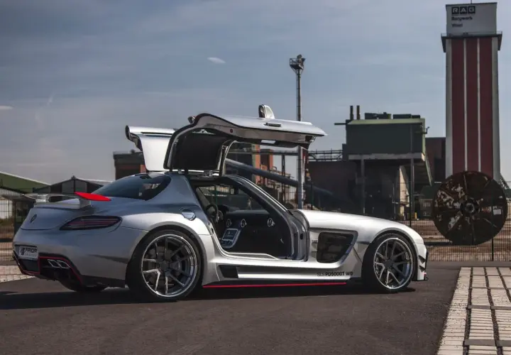 Srebrny SLS z otwartymi drzwiami typu gullwing, z czerwonym akcentem na spojlerze, zaparkowany przed industrialnym budynkiem.
