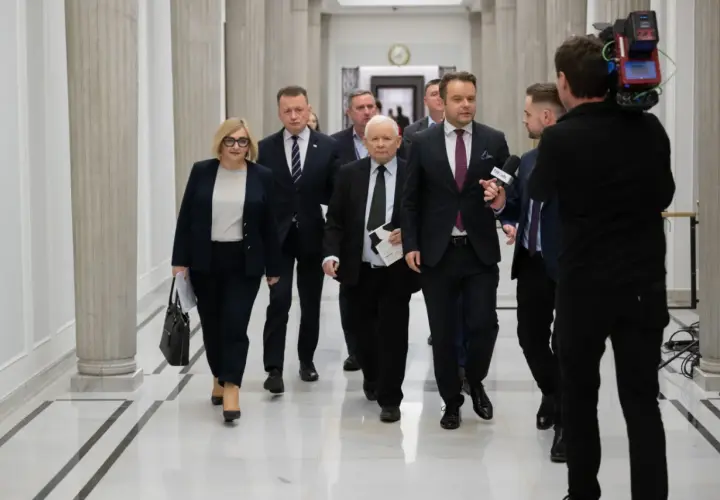 Politycy idą korytarzem, a kamerzysta nagrywa ich z tyłu. Widać, że idą w przeciwnych kierunkach, co jest ciekawe.