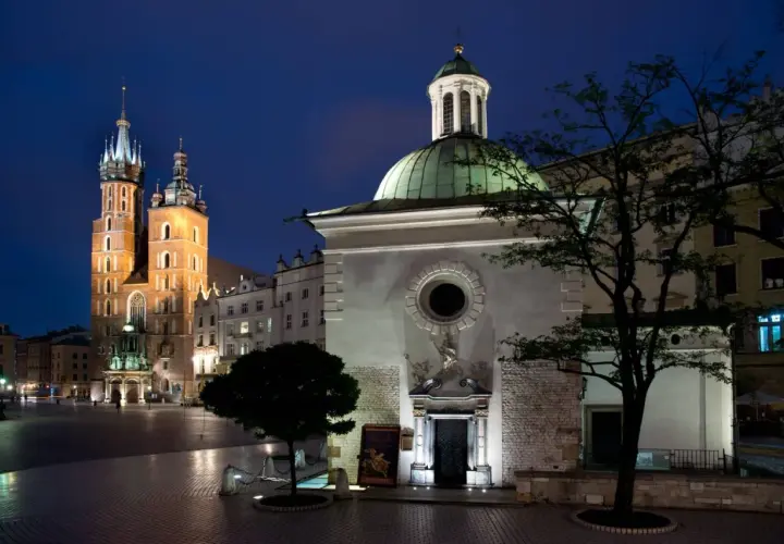 Nocny widok na Rynek Główny w Krakowie. W oddali majestatyczna Bazylika Mariacka, a na pierwszym planie kościół św. Wojciecha z zieloną kopułą.