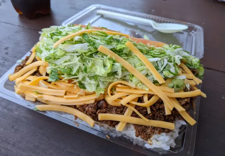 A hearty Okinawa taco rice dish, layered with white rice, seasoned ground meat, shredded lettuce, and melted cheese, ready to be enjoyed.