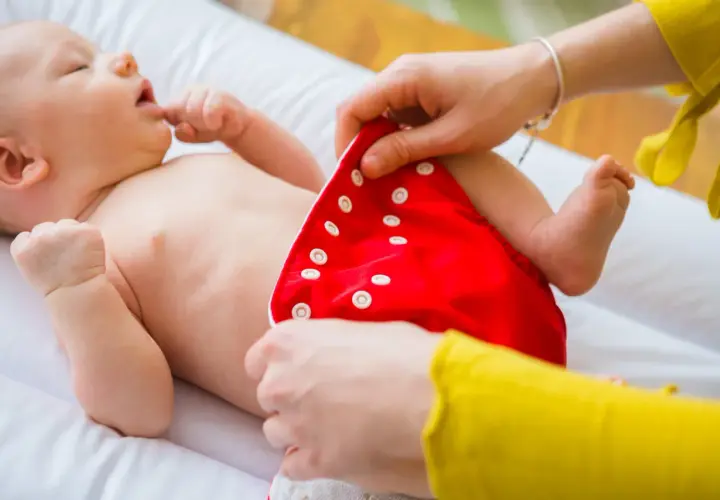 Mama zakłada dziecku czerwoną pieluchę tetrową. To pierwszy krok do tego, jak prać pieluchy tetrowe, by były czyste i ekologiczne.