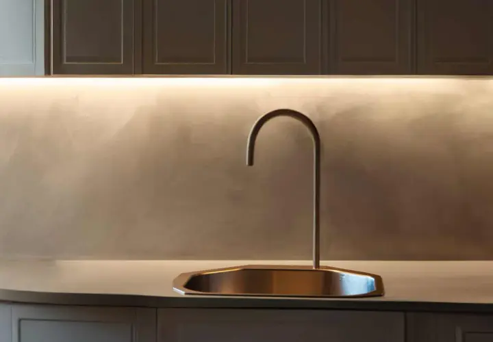 Rubinetto moderno su lavello in rame, con illuminazione a LED che valorizza la fascia di tamponamento cucina in resina spatolata.