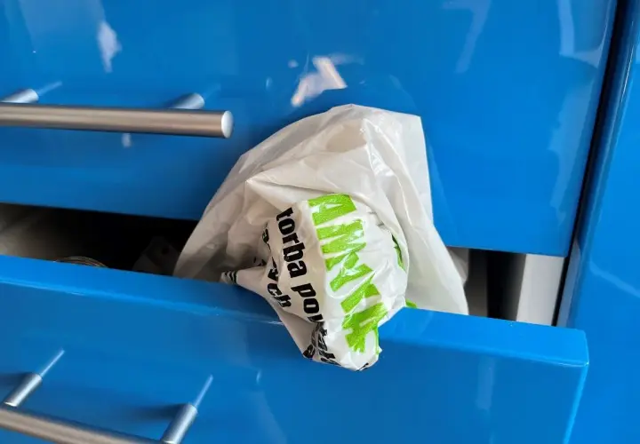 Biała reklamówka z zielonym napisem "Torba" wystaje z niebieskiej szuflady. Oto praktyczny sposób, jak przechowywać reklamówki.