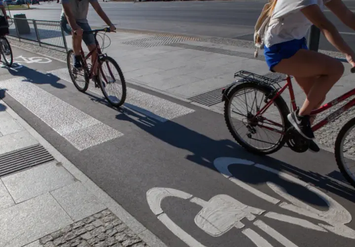 Ludzie na rowerach jadą ścieżką rowerową z oznaczeniem art 33 prd. Cienie rzucane przez rowerzystów wydłużają się na asfalcie.