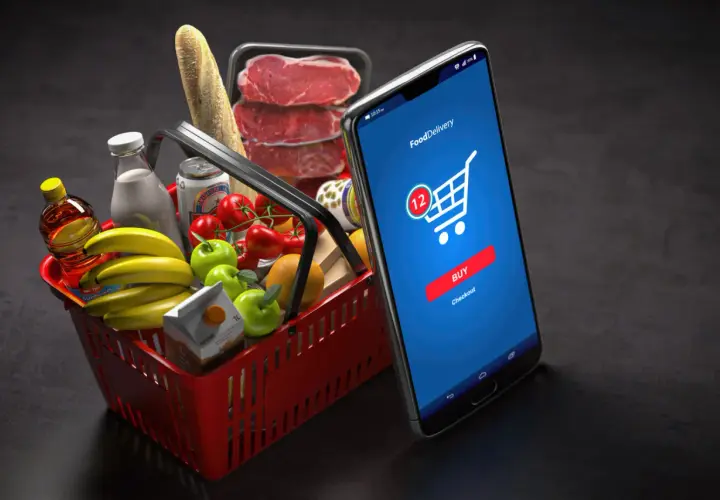 Koszyk z zakupami i smartfon z aplikacją do zamawiania jedzenia. M-commerce ułatwia zakupy spożywcze.