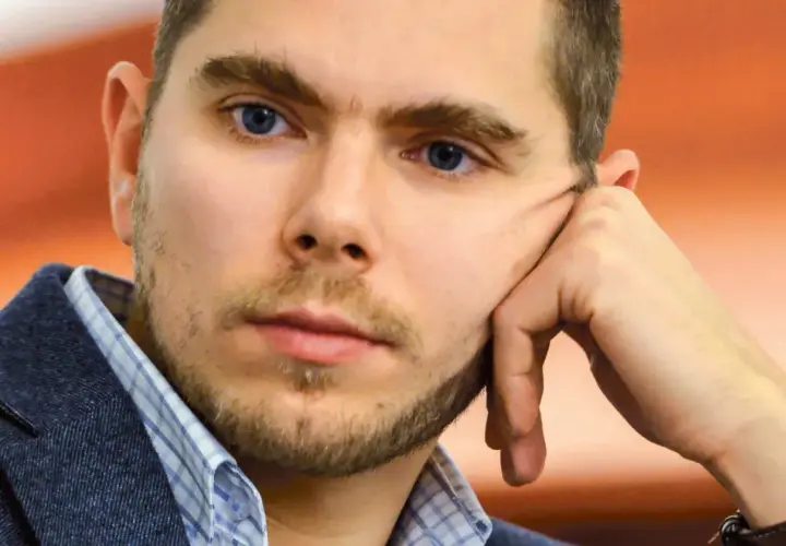 Portret Piotra Zychowicza, mężczyzny z niebieskimi oczami, opierającego głowę na dłoni.