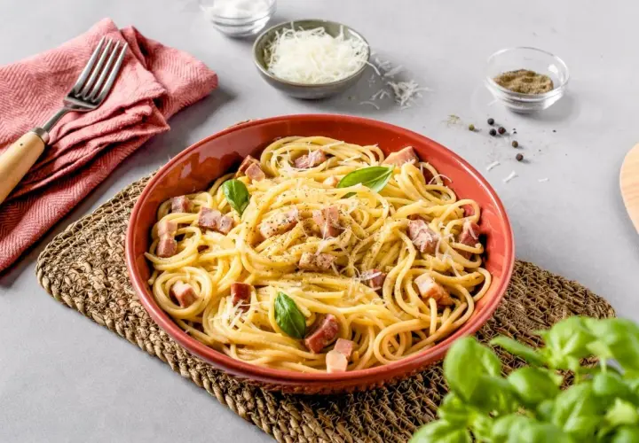 Un plato de carbonara italia, con espagueti, trozos de panceta, queso rallado y hojas de albahaca fresca.