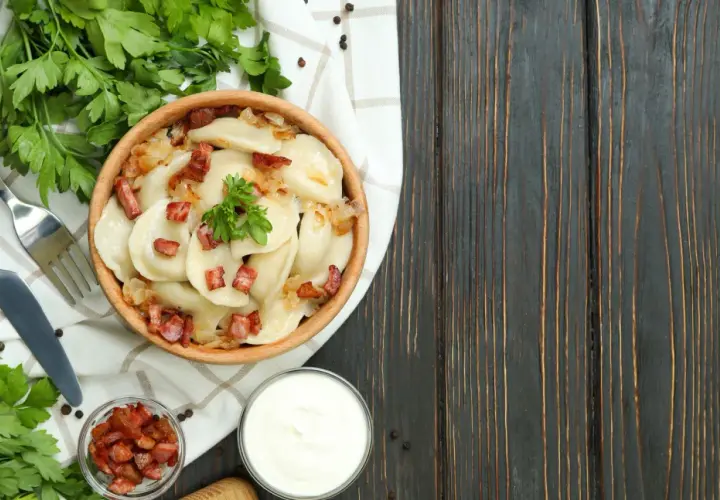 Pyszne pierogi z cebulką i skwarkami, serwowane w drewnianej misce. To klasyka kuchni łemkowskiej, podana z kwaśną śmietaną i świeżą natką pietruszki.
