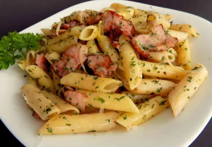 Pyszny makaron penne z kawałkami wędzonego boczku i posypany natką pietruszki. Idealny makaron na obiad.