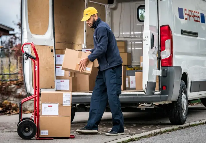 Zusteller lädt Pakete aus einem Lieferwagen. Viele Pakete, vielleicht wegen des peak season surcharge.