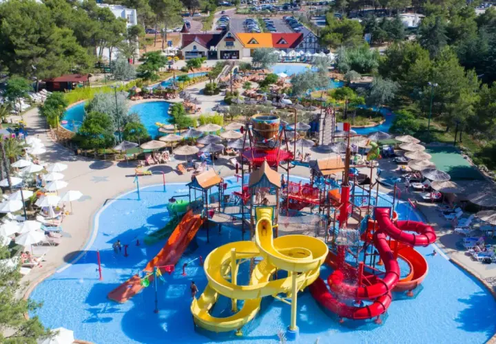 Un camping pour camping-car avec parc aquatique, offrant toboggans colorés, piscines et parasols pour des vacances en famille sous le soleil.